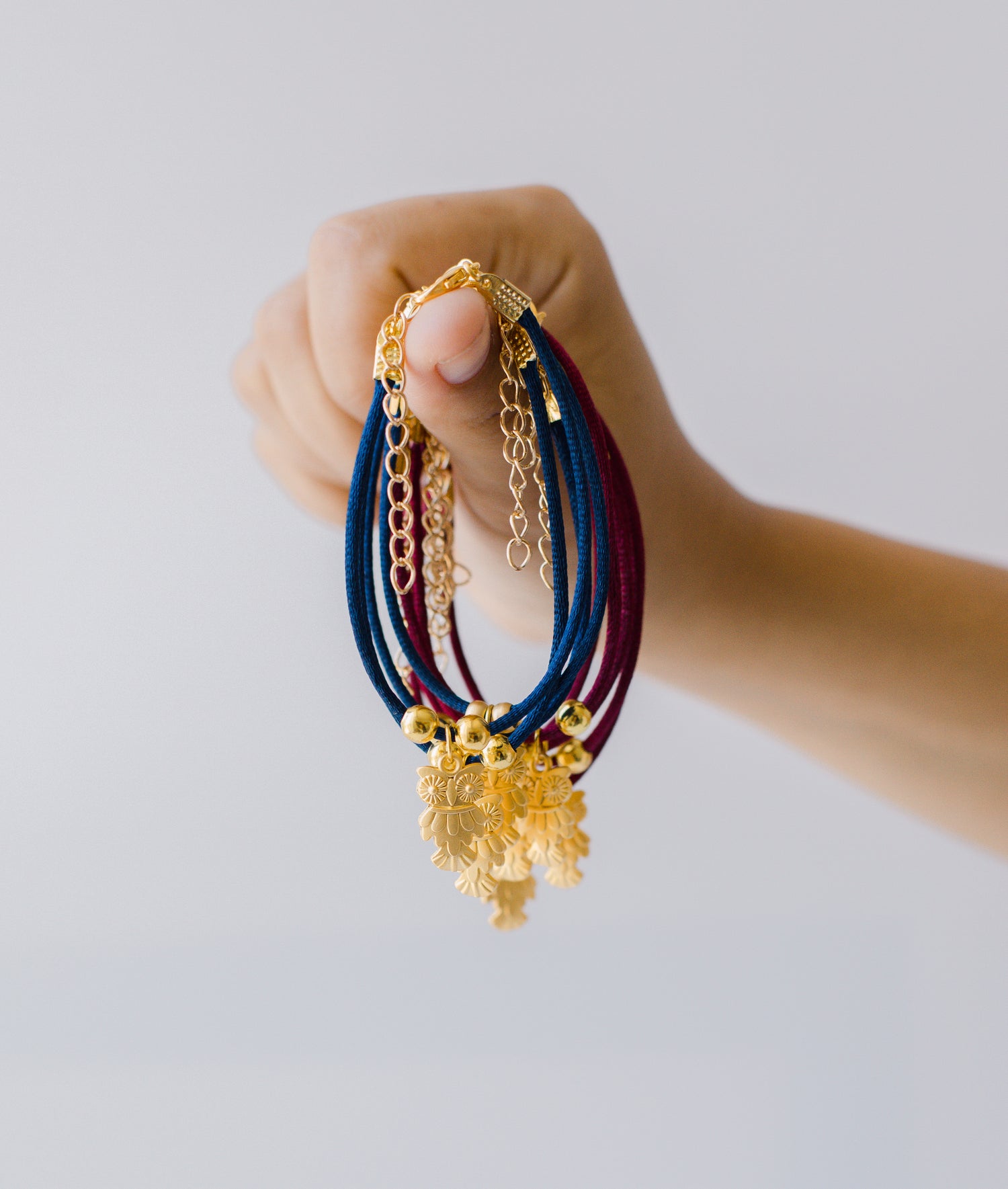 Hand hält ein Bündel Armbänder mit blauen und roten Bändern und goldfarbenen Anhängern und Ketten