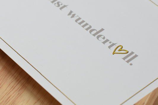 Detail einer weißen Postkarte mit dem Text 'Du bist wundertoll.' und einem goldfarbenen Herzsymbol