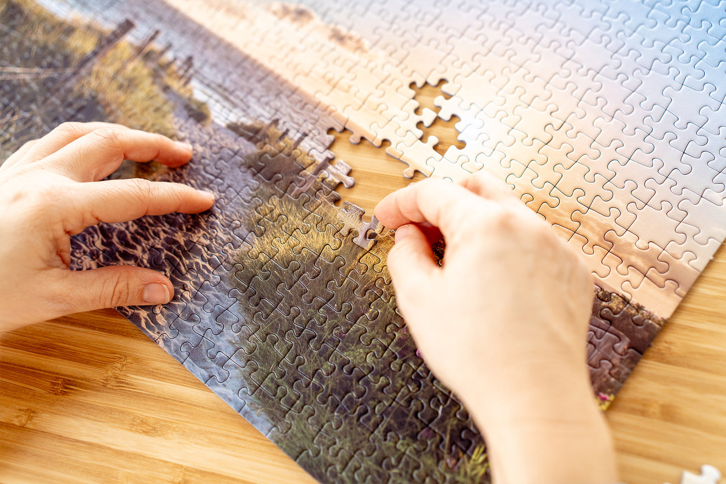 Hände setzen ein fehlendes Puzzlestück in ein Landschaftspuzzle mit Küstenmotiv ein