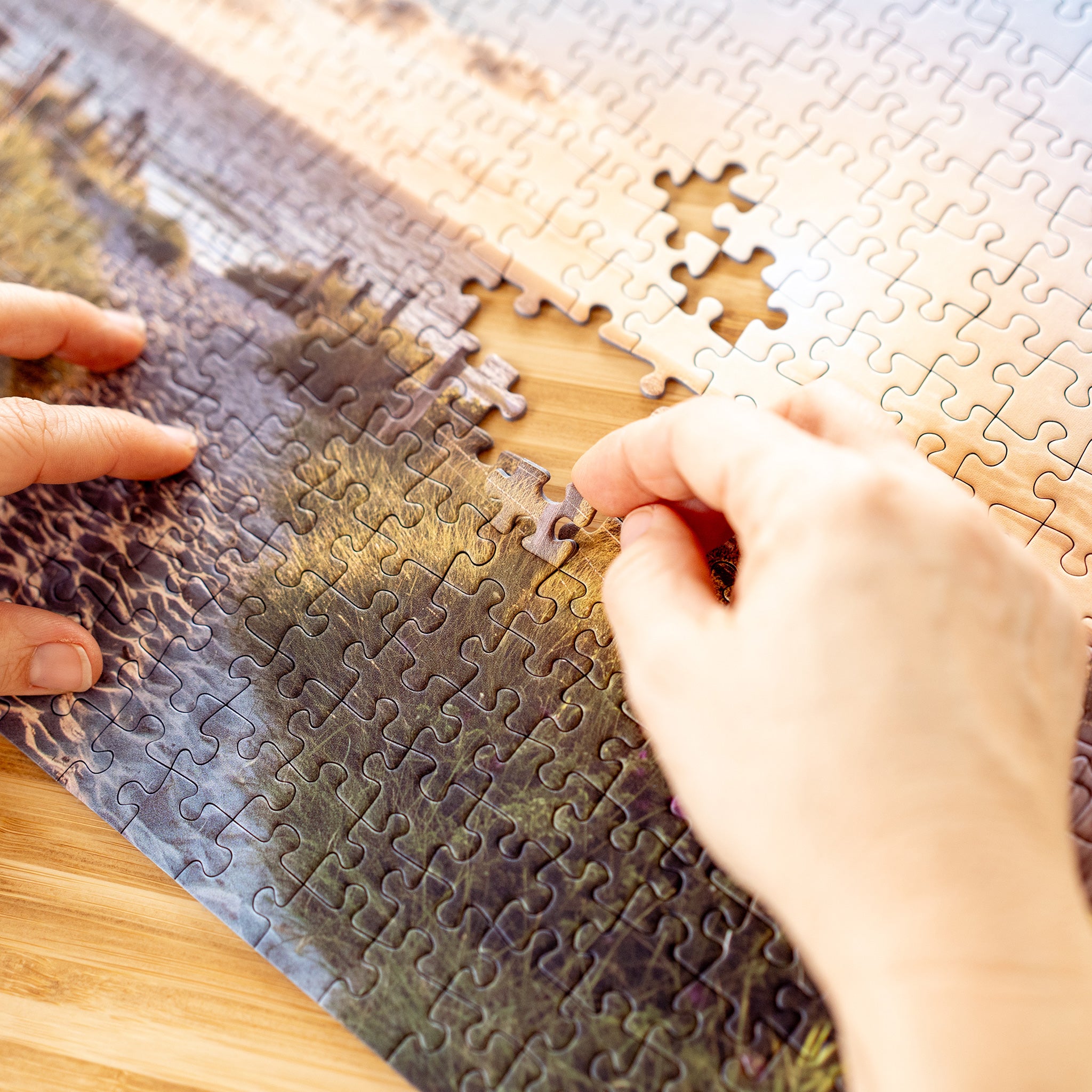 Hände setzen ein fehlendes Puzzlestück in ein Landschaftspuzzle mit Küstenmotiv ein