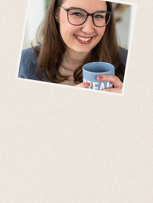 Lächelnde Frau mit Brille hält eine blaue Tasse mit der Aufschrift 'DREAM'