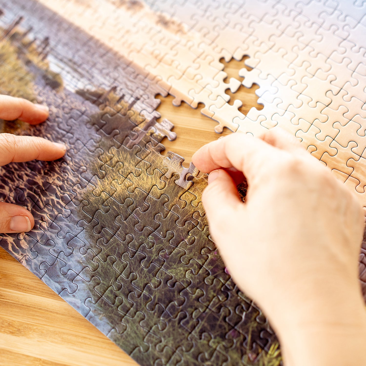 Hände setzen ein fehlendes Puzzlestück in ein Landschaftspuzzle mit Küstenmotiv ein